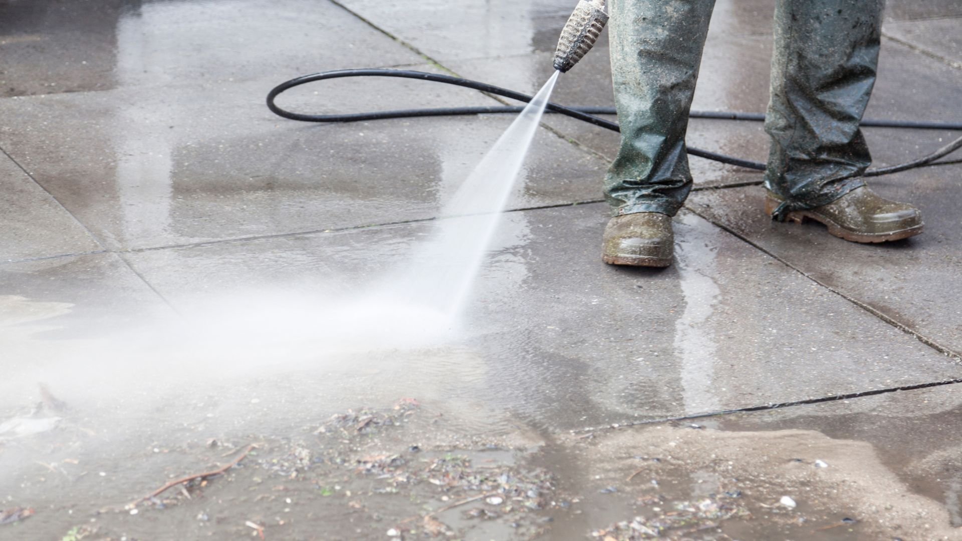Person pressure washing concrete surface with high-pressure water spray