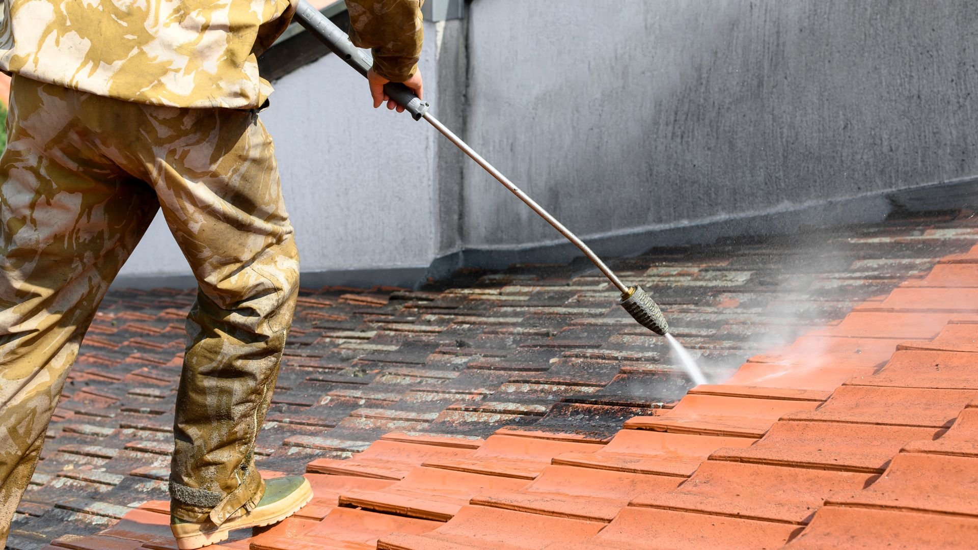 Person in camouflage using high-pressure washer to clean terracotta tiles