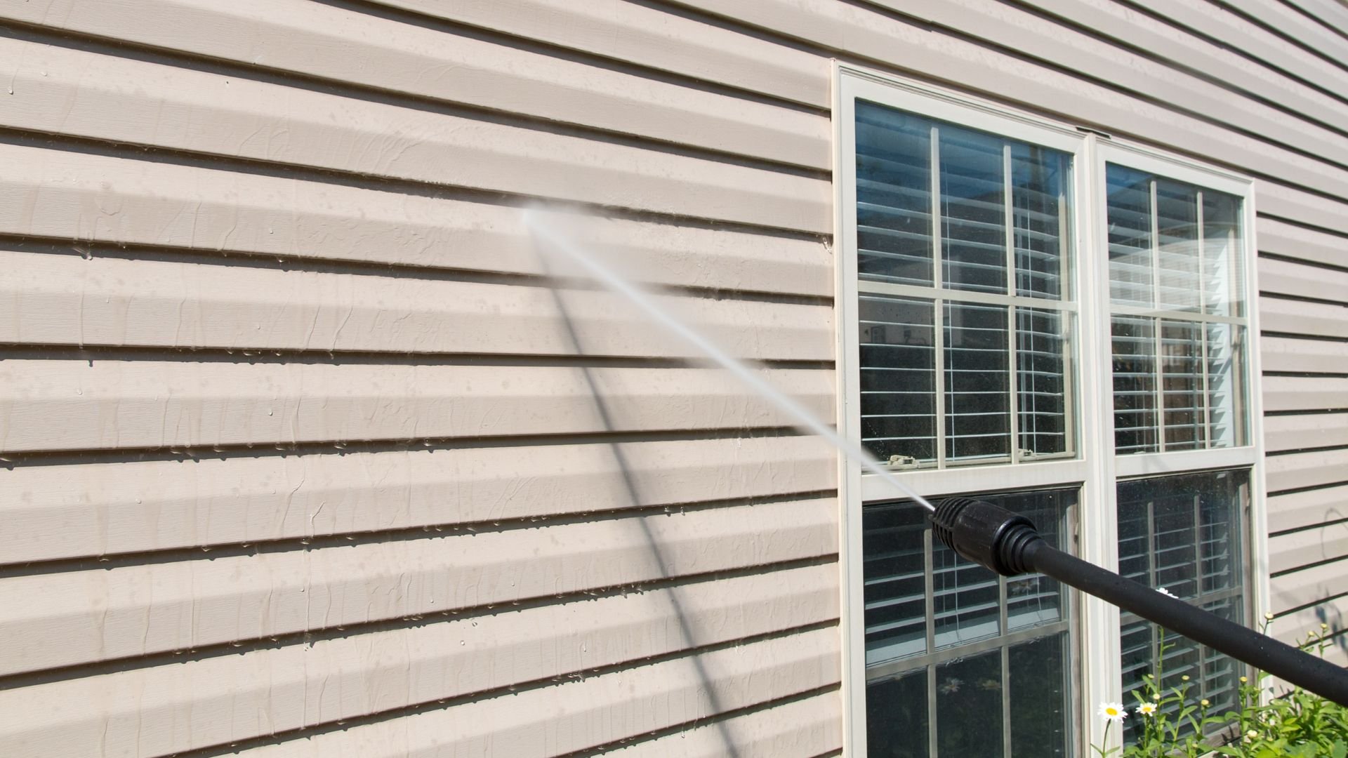 Power washer cleaning vinyl siding near white windows with blinds