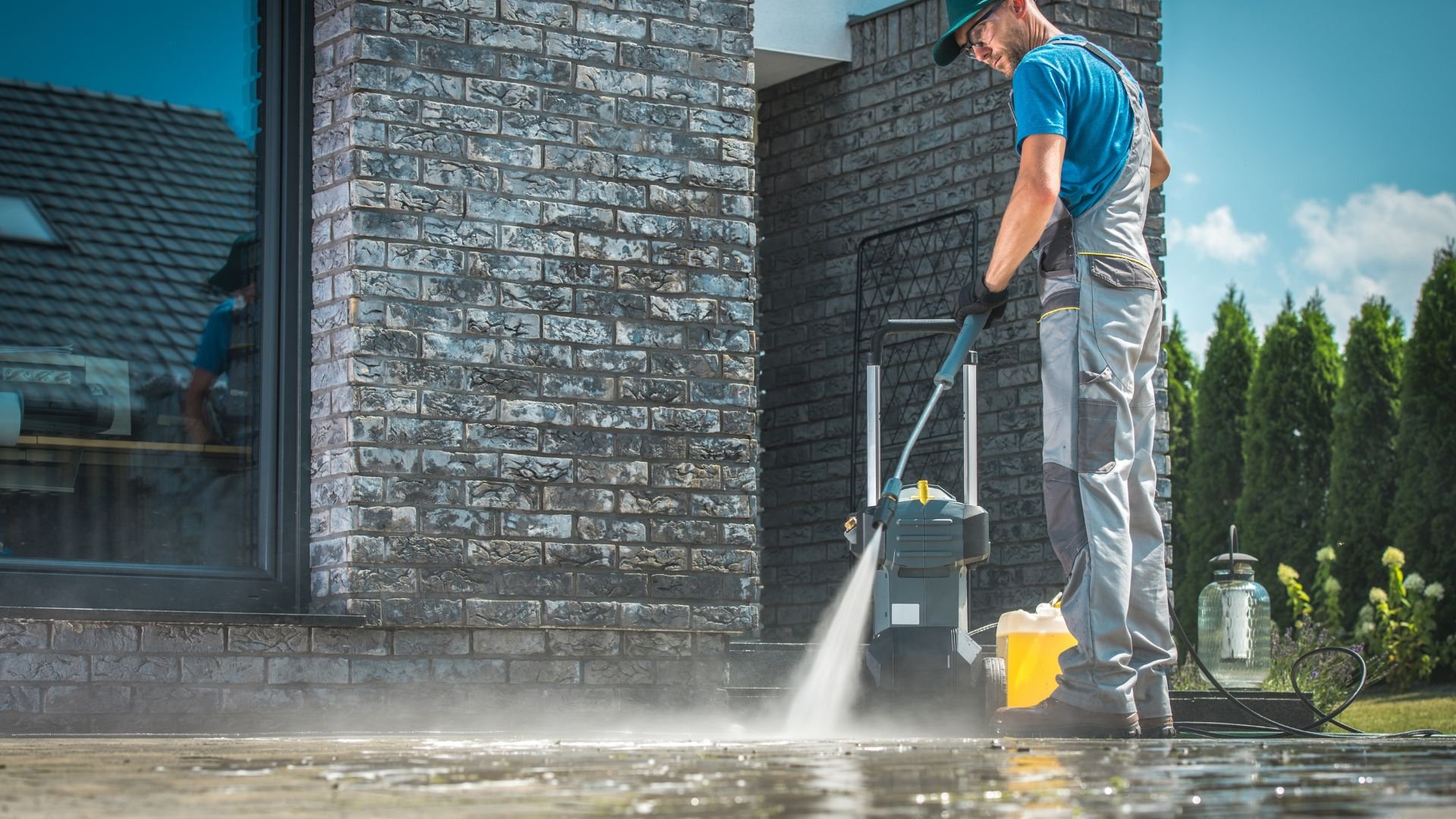 Professional using pressure washer to clean exterior brick wall and concrete