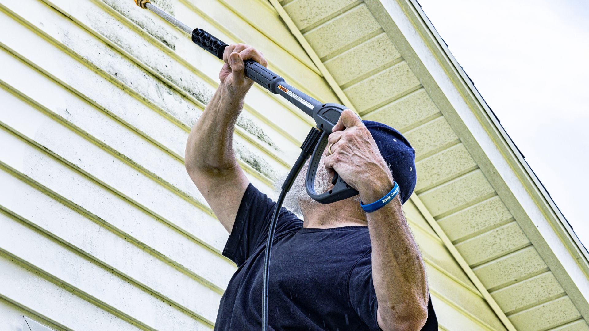 Person using pressure washer to clean siding of a house