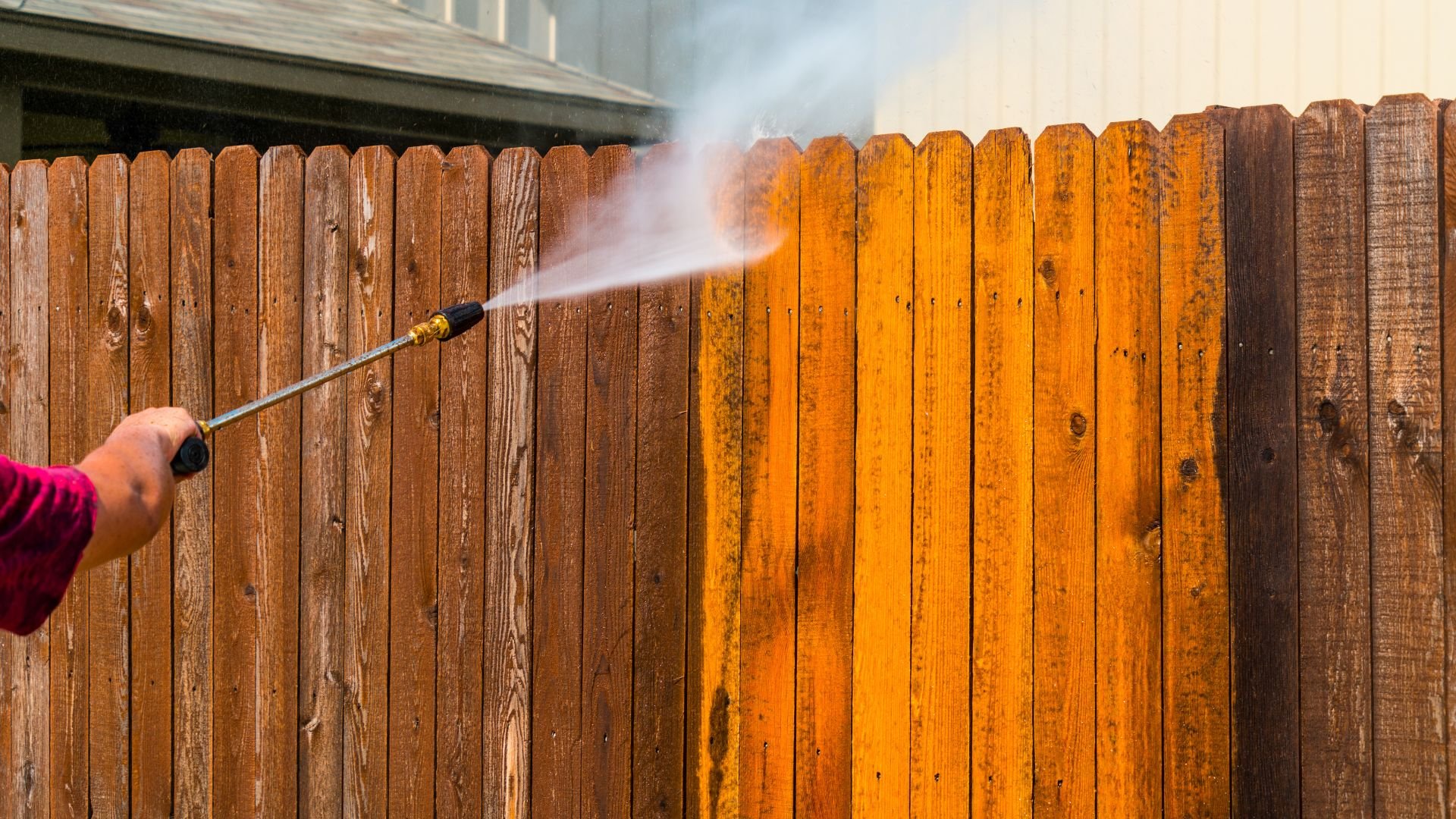 Pressure washer cleaning wooden fence, revealing bright wood color