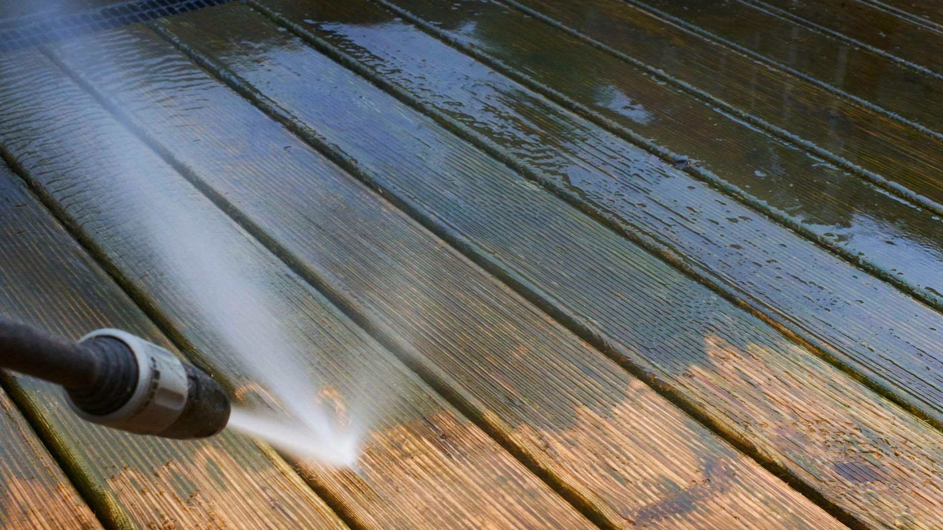 Power washer cleaning wooden deck, spraying water and removing dirt
